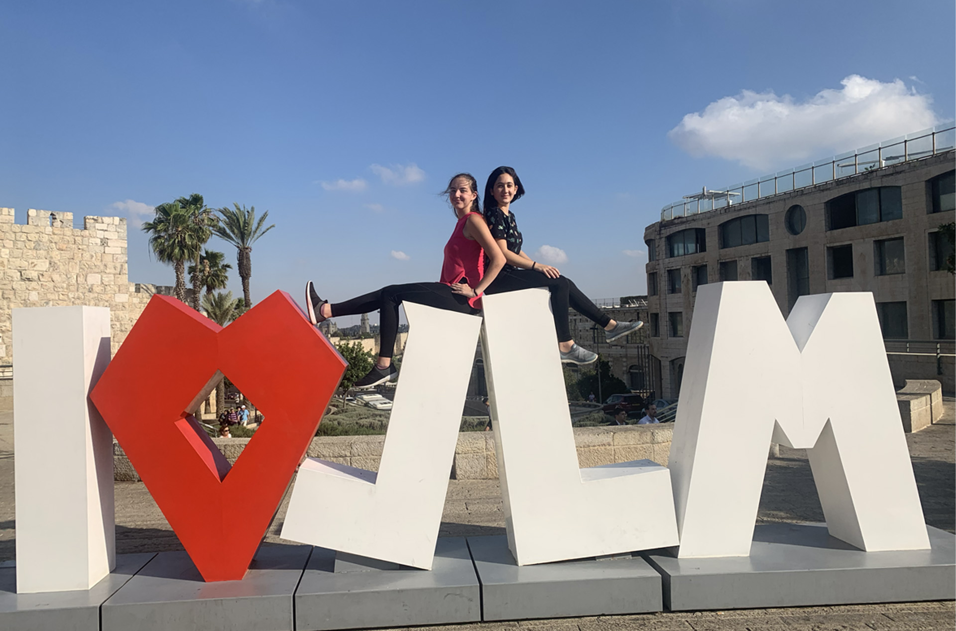 Two girl sitting on big clock letters that say I heart JLM (jerusalem)